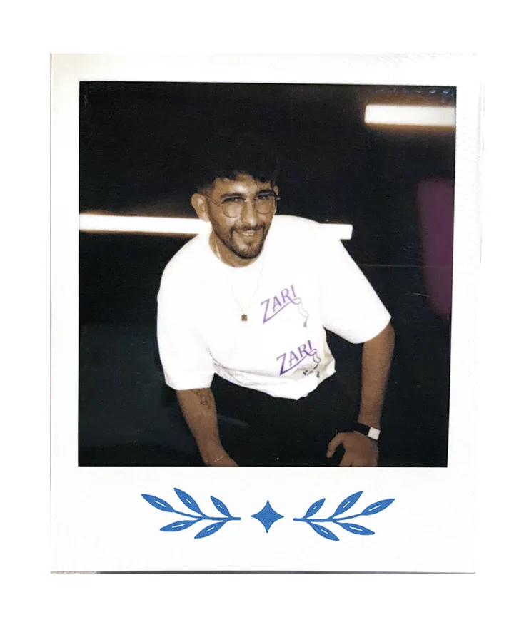 A member seated under a strip light, in the Zari tee.