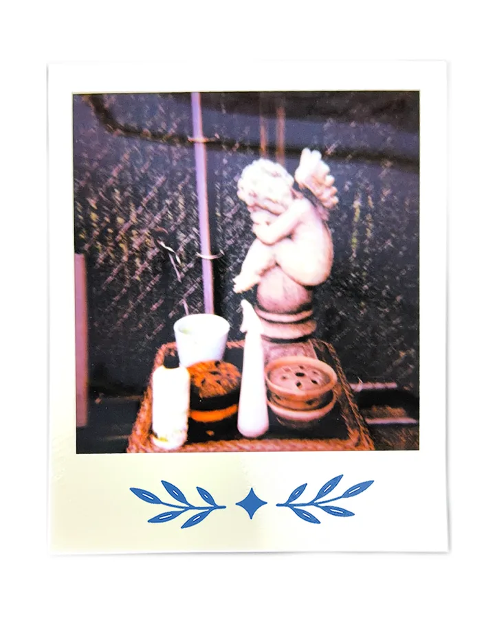 A plaster cherub on a garden table, beside cups and a bottle.