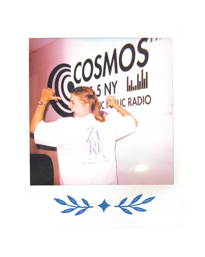 A member in the Zari tee, arm raised, the Cosmos FM sign behind.